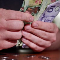 Des billets d'argent dans une main et de la monnaie sur la table.