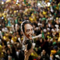 Une foule immense est réunie en arrière-plan. Le focus de la photo est fait sur une petite affiche représentant Bolsonaro.
