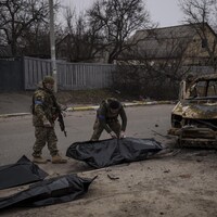 Trois soldats se tiennent près de sacs de plastique qui contiennent des corps.
