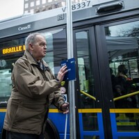 Une personne malvoyante utilise une signalisation en braille devant un autobus.