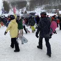 Des amateurs de sport d'hiver, planches à la main, à travers la foule au bas de la montagne. 
