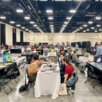 Des gens jouent à des jeux de société autour de tables installées dans une grande salle ouverte.