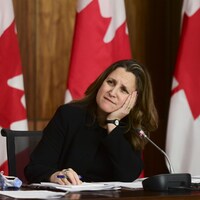 Assise à un bureau la tête appuyée dans la paume de sa main, Chrystia Freeland écoute la question d'un journaliste.