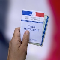 Une personne tient dans sa main une carte électorale ainsi qu'une pièce d'identité.