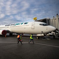 Un employé transportant du désinfectant aérien passe devant un avion 737-800 (738) de la compagnie aérienne canadienne WestJet, à la rampe d’embarquement 17 de l'Aéroport international de Vancouver (YVR) à Richmond, en Colombie-Britannique, le jeudi 21 janvier 2021.