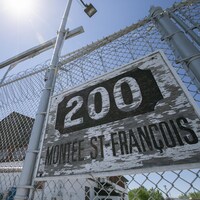 Une clôture à mailles de chaîne coiffée de barbelés, portant l'adresse « 200, montée Saint-François ».