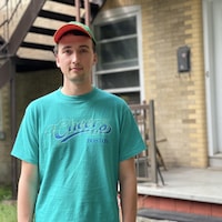 Un jeune homme portant une casquette et un chandail turquoise regarde l'objectif.