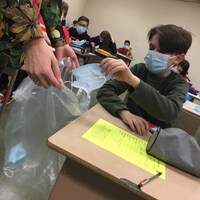 Un élève met sont vieux masque dans un sac de poubelle. 