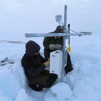 David Burgess et Bradley Danielson, emmitouflés, recueillent les données d'une station météorologique.