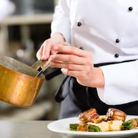 Un chef dispose de la sauce dans un plat de viande dans une cuisine de restaurant. 