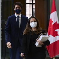 Chrystia Freeland, masquée, tenant des documents, marche, suivie de Justin Trudeau, également masqué.