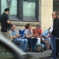 Des citoyens assis sur des chaises de camping sur un trottoir, à Montréal, devant un édifice.