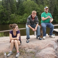 Une fille avec deux garçons assis sur une roche sous le soleil. 