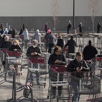 Des clients font la file avec des paniers dans le stationnement d'un commerce.