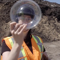Une femme tient un plat de plastique près d'un tas de compost.