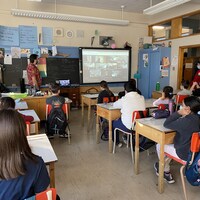 Des élèves dans une classe qui écoutent un athlète sur un écran. 