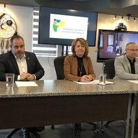 Martin Ferron, Diane Dallaire et Sébastien D'Astous derrière une table lors d'un point de presse, Claire Bolduc dans un écran de visioconférence.