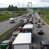 Des voitures circulent au ralenti sur l’autoroute Henri-IV, en direction sud, à l’approche du pont Pierre-Laporte, qu’on aperçoit au loin. Le pont de Québec est également visible à gauche. La photo a été prise de jour l'été.