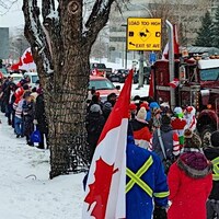 Un gros camion entouré de manifestants brandissant des drapeaux du Canada, un jour d'hiver.