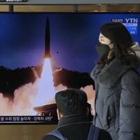 Une femme passe devant un écran montrant un missile qui décolle.