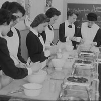De jeunes filles en tablier cuisinant le long d'une table dans une classe.