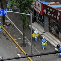 Des travailleurs de la santé vêtus de combinaison sanitaire marchent dans un quartier de Shanghai.