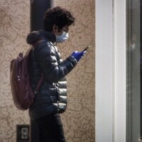 Une personne regarde son téléphone avec un masque au visage et des gants.