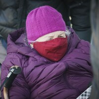 Une dame âgée porte bonnet, couvre-visage et manteau d'hiver.