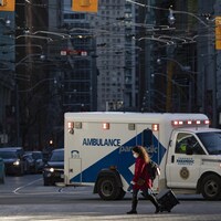 Une ambulance roule dans les rues de Toronto pendant qu'une piétonne portant un masque traverse la rue.