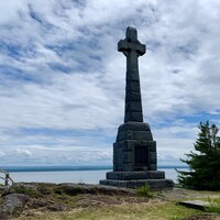 Une croix de pierre érigée devant le fleuve Saint-Laurent.