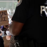 Une jeune femme brandit une pancarte où il est écrit « Defund the Police » devant un agent torontois.