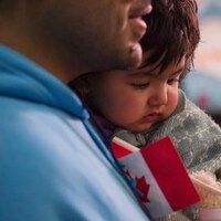 Une petite fille dans les bras de son père qui tient un petit drapeau canadien