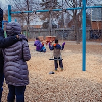 Un couple, de dos, regarde trois enfants assis dans les balançoires d'un parc.