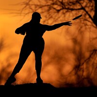 Silhouette d'une femme sur un fond orange. Elle lance un frisbee dans un parc.