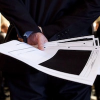 Un fonctionnaire fédéral tient dans une main des feuilles d'un document censuré. 