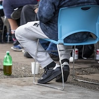 Des personnes assises sur des chaises disposées en cercle avec des bouteilles et des cannettes d'alcool à terre à leurs pieds.