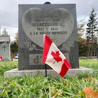 Un drapeau canadien est planté devant une pierre tombale.