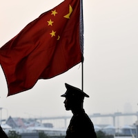 Des soldats chinois passent à côté d'un drapeau de la Chine.