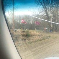 Deux drapeaux flottent à l'entrée d'une propriété, au loin.