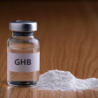 Une bouteille de GHB liquide et en poudre sur un comptoir de bois.