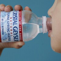 Un enfant boit au goulot d'une bouteille d'eau de source.