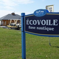 Une affiche indique la base nautique Écovoile. Derrière, un bâtiment de services ainsi que des bateaux.