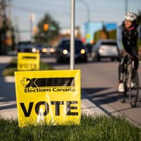 Un homme en vélo passe devant une affiche jaune d'Élections Canada plantée dans une pelouse.