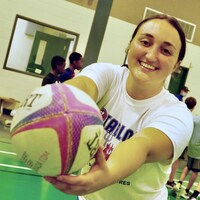 Elizabeth Gaspo qui tient un ballon de rugby dans un gymnase où se trouvent des enfants.