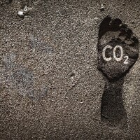 Marque laissée par un pied dans le sable, accompagnée par la formule chimique du gaz carbonique, représentant l'empreinte humaine sur le climat de la planète
