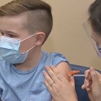 L'enfant regarde au loin pendant qu'on lui injecte le vaccin dans le bras.