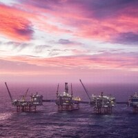 Des plateformes pétrolières en mer sous un ciel rose et mauve