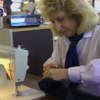 Une femme devant une machine à coudre avec une pièce de tissu dans les mains.