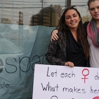 Deux femmes tiennent une pancarte devant une vitre dans la rue. 
