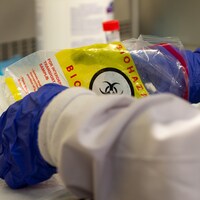 Les mains gantées d'une technologue du laboratoire sortent un tube de prélèvement d'un sac pour matière à biorisques.